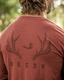 Red shirt with deer antler and duck design on the back, labeled 'Decoy', against a blurred natural background.