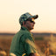 A man hunting while wearing the Frogskin Camo Preservation Rope Hat in the early morning sunrise.